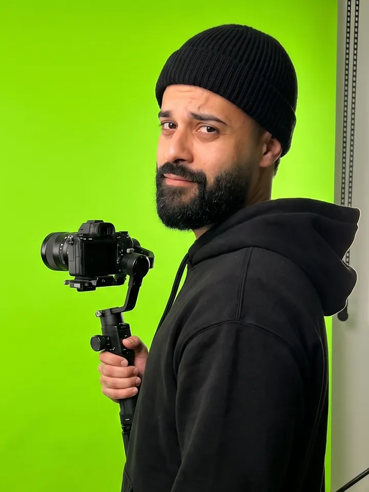 Israel Meira de gorro preto, com uma câmera num gimbal, olhando por cima do ombro, num estúdio de fundo verde