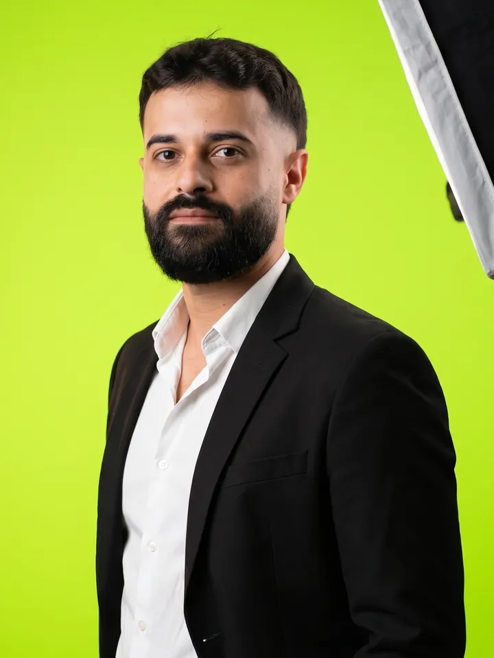 Israel Meira de blazer preto e camisa branca, num estúdio de fundo verde